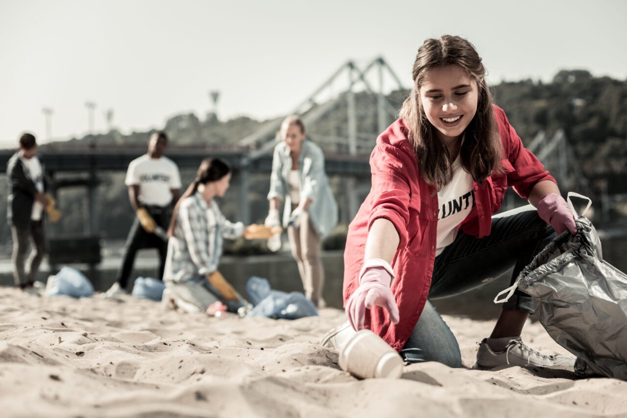 young dark haired student wearing red anorak putting cups into garbage bag